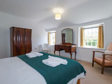 A bedroom with a bed covered with green blanket and towels wardrobe dressing table and two chairs at Pennine in Veryan