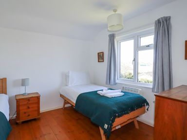 A bedroom with two single beds a wooden bedside table with a lamp a window with curtains and a wooden dresser at Pennine in Veryan