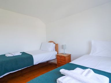 A bedroom with two single beds a wooden nightstand and a small lamp at Pennine in Veryan