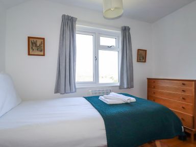 A bedroom with a bed covered with white linen and dark green blanket beside a wooden dresser at Pennine in Veryan