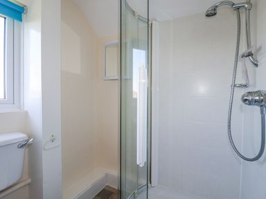 A bathroom with a toilet, window, curved glass shower door, and a shower with a handheld showerhead at Pennine in Veryan