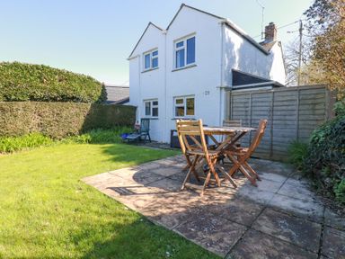 An outdoor patio with wooden table and chairs on a stone floor next to a two story white house at Pennine in Veryan