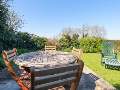 A garden with a round wooden table and chairs on a stone patio and a green reclining chair on the grass at Pennine in Veryan