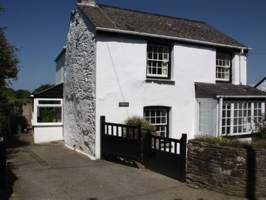 A white stone house with black-trimmed windows and a black gate in front at Pennine in Veryan