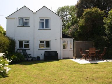 A white two story house with a garden and outdoor seating area with wooden table and chairs at Pennine in Veryan