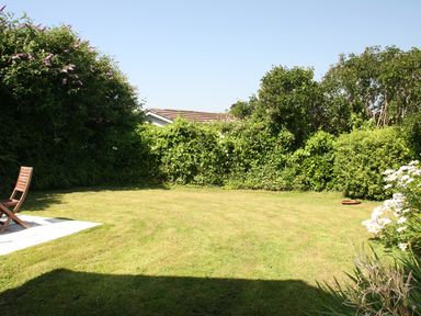 A garden with a wooden chair on a small patio surrounded by bushes and flowers at Pennine in Veryan