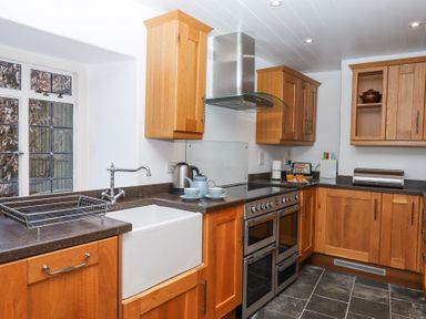 A kitchen with wooden cabinets a double oven a white sink and a window at 2 New Mill Cottages in North Bovey