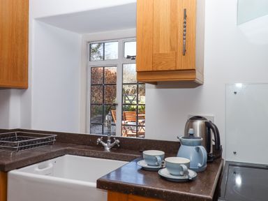 A kitchen sink with faucet under a window overlooking an outdoor seating area with wooden chairs and table at 2 New Mill Cottages in North Bovey