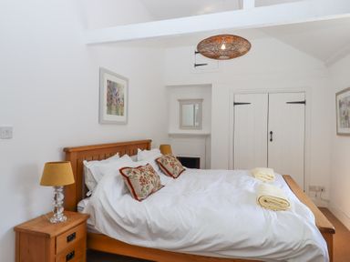 A bedroom with a wooden bed with white bedding and decorative pillows at 2 New Mill Cottages in North Bovey