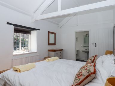 A bedroom with a bed, window, dresser, mirror, and bathroom at 2 New Mill Cottages in North Bovey