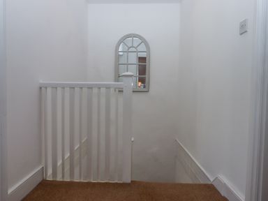 A staircase with white railing and a wall mirror at 2 New Mill Cottages in North Bovey