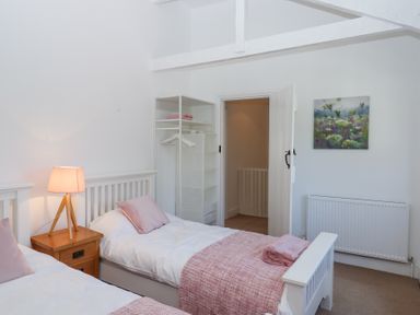 A bedroom with two single beds bedside table with lamp open doorway and a painted canvas at 2 New Mill Cottages in North Bovey