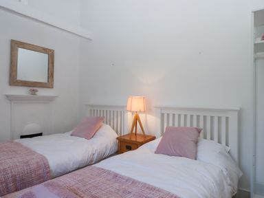 A bedroom with two single beds with pink pillows and blankets and a wooden lamp on a bedside table at 2 New Mill Cottages in North Bovey