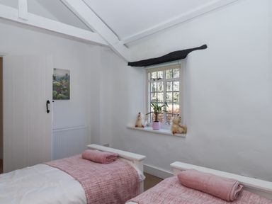 A bedroom with two single beds with pink blankets and towels near a window with a plant and decorative items at 2 New Mill Cottages in North Bovey