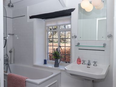 A bathroom with a bathtub shower and a sink under a mirror at 2 New Mill Cottages in North Bovey