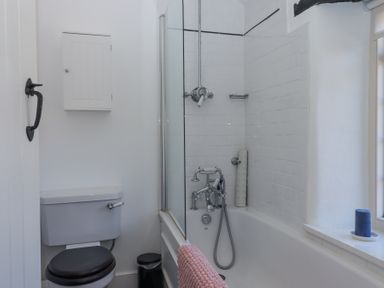 A bathroom with a toilet and bathtub with shower at 2 New Mill Cottages North Bovey
