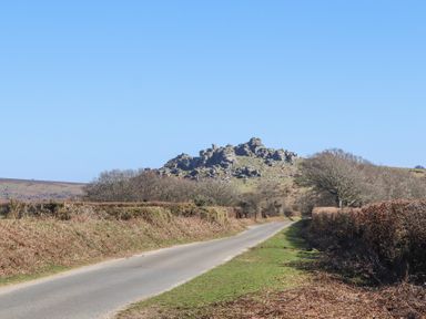 A country road with hedges and leafless trees leading to rocky hills under a clear sky at 2 New Mill Cottages in North Bovey