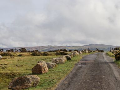 A rural road bordered by large stones and grassy fields with hills in the background at 2 New Mill Cottages in North Bovey