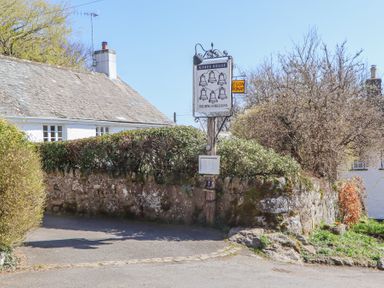 A street view showing a stone wall with bushes and a sign for The Ring of Bells Inn at 2 New Mill Cottages in North Bovey