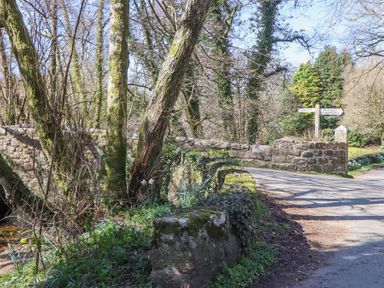 A stone bridge with trees and vegetation near a road sign at 2 New Mill Cottages North Bovey