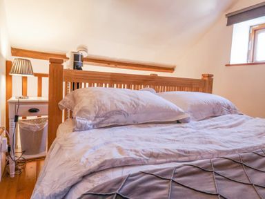 A bedroom with a wooden bed frame pillows and bedding a bedside table with a lamp and a waste bin at The Yarde Annexe Pen Elm near Taunton