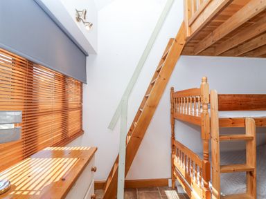 A small bedroom with wooden bunk beds a wooden chest of drawers and stairs leading to a loft at The Yarde Annexe in Pen Elm near Taunton