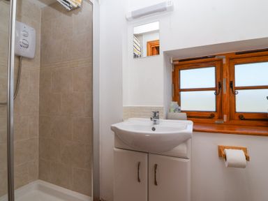 A bathroom with a shower cubicle a sink cabinet a mirror a wooden window and a toilet paper holder at The Yarde Annexe Pen Elm near Taunton