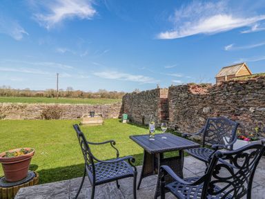 A garden patio with black metal chairs and table with a bottle and glass near a stone wall at The Yarde Annexe in Pen Elm near Taunton