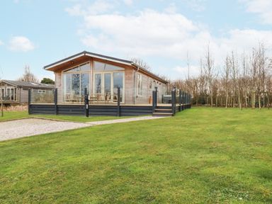 A wooden cabin with large glass windows and a deck surrounded by glass railings on a grassy lawn at 6 Meadow Retreat in Dobwalls