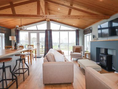 A living room with sofas armchair ottoman wood stove and large windows at 6 Meadow Retreat in Dobwalls