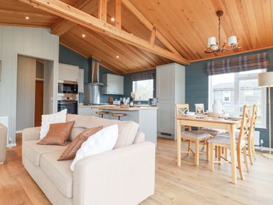 An open living area with a beige sofa and pillows a kitchen with stools and dining table with chairs at 6 Meadow Retreat in Dobwalls