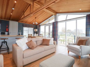A living room with sofa and armchair next to large sliding glass doors with blue plaid curtains at 6 Meadow Retreat in Dobwalls