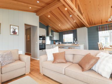 A living room with beige sofas and cushions next to an open kitchen with white cabinets and wooden ceiling at 6 Meadow Retreat in Dobwalls