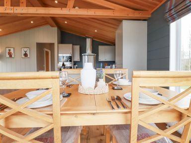 A dining table set with plates glasses and cutlery in an open kitchen area with wooden ceiling and cabinets at 6 Meadow Retreat in Dobwalls