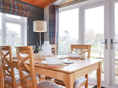 A dining area with a wooden table set for four near large windows and glass doors at 6 Meadow Retreat in Dobwalls