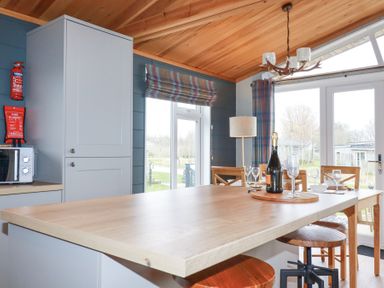 A dining area with a wooden table set with glasses and a bottle near large windows and a door at 6 Meadow Retreat Dobwalls