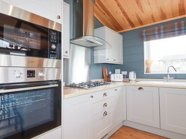 A kitchen with wooden ceiling white cabinets gas stove oven microwave and window at 6 Meadow Retreat in Dobwalls