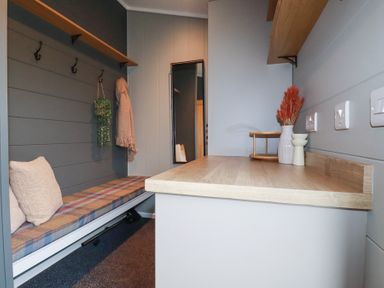 A small mudroom with a wooden bench with cushions hooks on the wall and a wooden countertop decorated with a vase and shelves at 6 Meadow Retreat Dobwalls