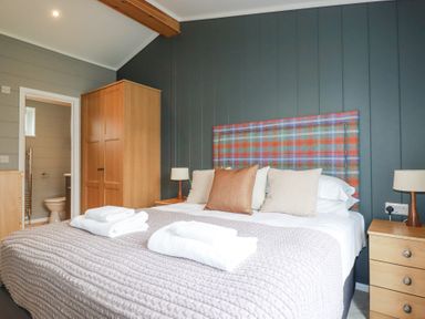 A bedroom with a bed with folded towels and cushions a wooden wardrobe and a bedside table with a lamp at 6 Meadow Retreat in Dobwalls