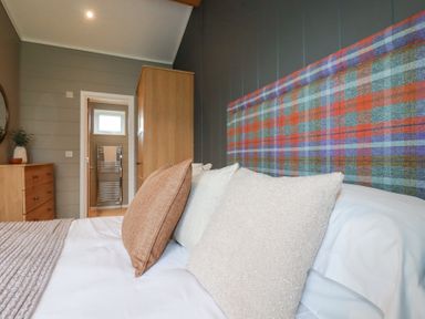 A bedroom with a bed with a plaid headboard and cushions next to wooden furniture at 6 Meadow Retreat in Dobwalls