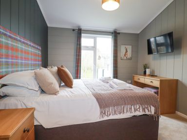 A bedroom with a bed and pillows a wooden desk a TV mounted on the wall and curtains at 6 Meadow Retreat in Dobwalls