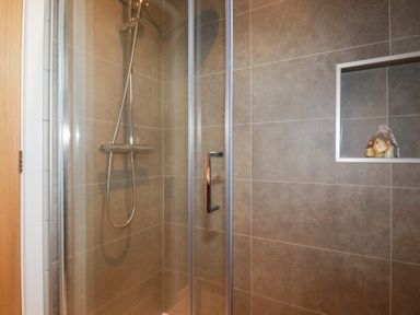 A shower cubicle with a glass door a handheld shower head and built in shelf with toiletries at 6 Meadow Retreat in Dobwalls