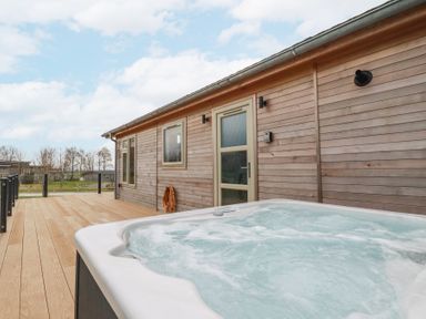 An outdoor wooden deck with a hot tub next to a cabin with a door and windows at 6 Meadow Retreat in Dobwalls