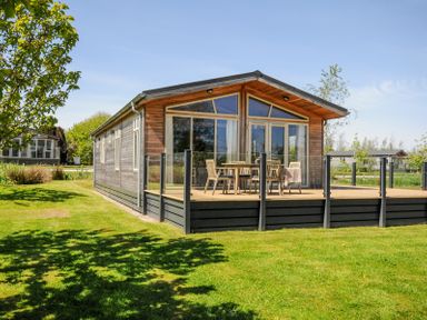 A wooden cabin with a glass enclosed deck and outdoor furniture on a grassy lawn at 17 Meadow Retreat in Dobwalls