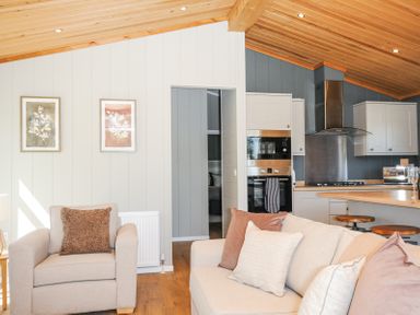 A living area with beige armchair and sofa with cushions next to a kitchen with bar stools at 17 Meadow Retreat in Dobwalls