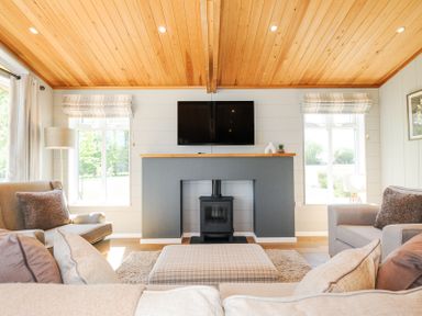A living room with a wooden ceiling a TV mounted above a fireplace and armchairs at 17 Meadow Retreat in Dobwalls