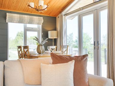 A dining area with a wooden table set with plates and glasses next to large glass doors and a sofa with cushions at 17 Meadow Retreat in Dobwalls