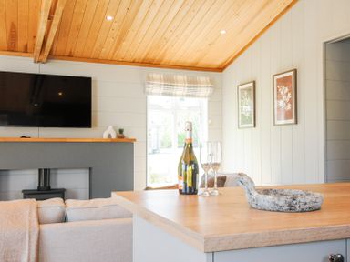 A living room with a mounted television above a fireplace and a kitchen counter with a bottle and two glasses at 17 Meadow Retreat in Dobwalls