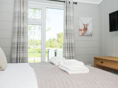 A bedroom with a bed covered in folded towels a wooden dresser a wall-mounted television and a deer painting at 17 Meadow Retreat in Dobwalls