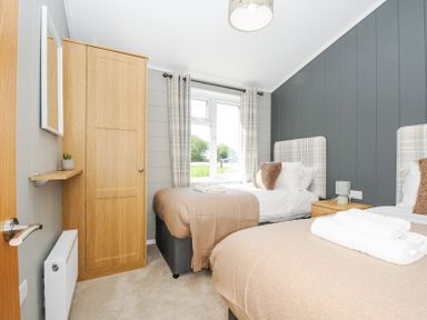 A bedroom with two single beds a wooden wardrobe and a window with plaid curtains at 17 Meadow Retreat in Dobwalls